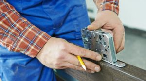 zoom sur un serrurier entrain de poser une serrure sur une porte en bois