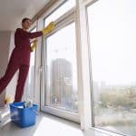Joyous woman standing on windowsill and cleaning window