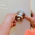 Male carpenter fixing lock in door with home